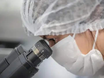 Científica mira a través de un microscopio en un laboratorio Científica mira a través de un microscopio en un laboratorio