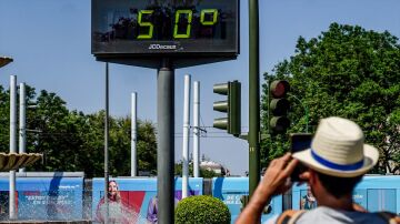Transeúntes fotografían el termómetro situado en el Prado (Sevilla) que marca 50 grados.