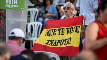 Una mujer muestra una bandera de España con el lema "que te vote Txapote" durante un mitin de Vox