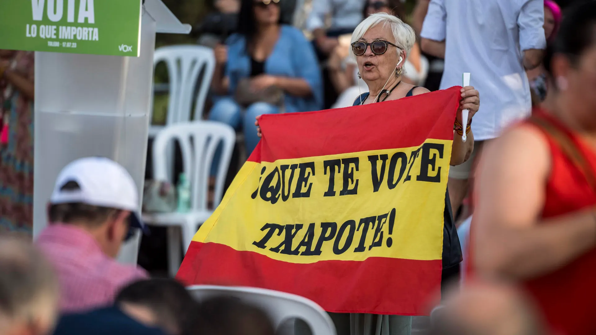 Una mujer muestra una bandera de España con el lema "que te vote Txapote" durante un mitin de Vox