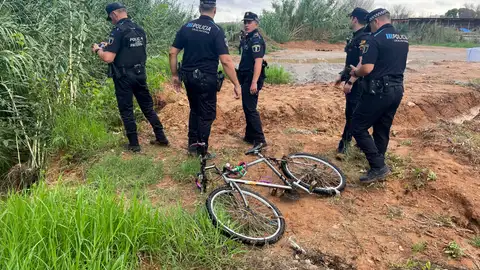 La Policía Local de paterna junto a la bicicleta del hombre arrastrado por el agua que intentó cruzar un barranco en Paterna