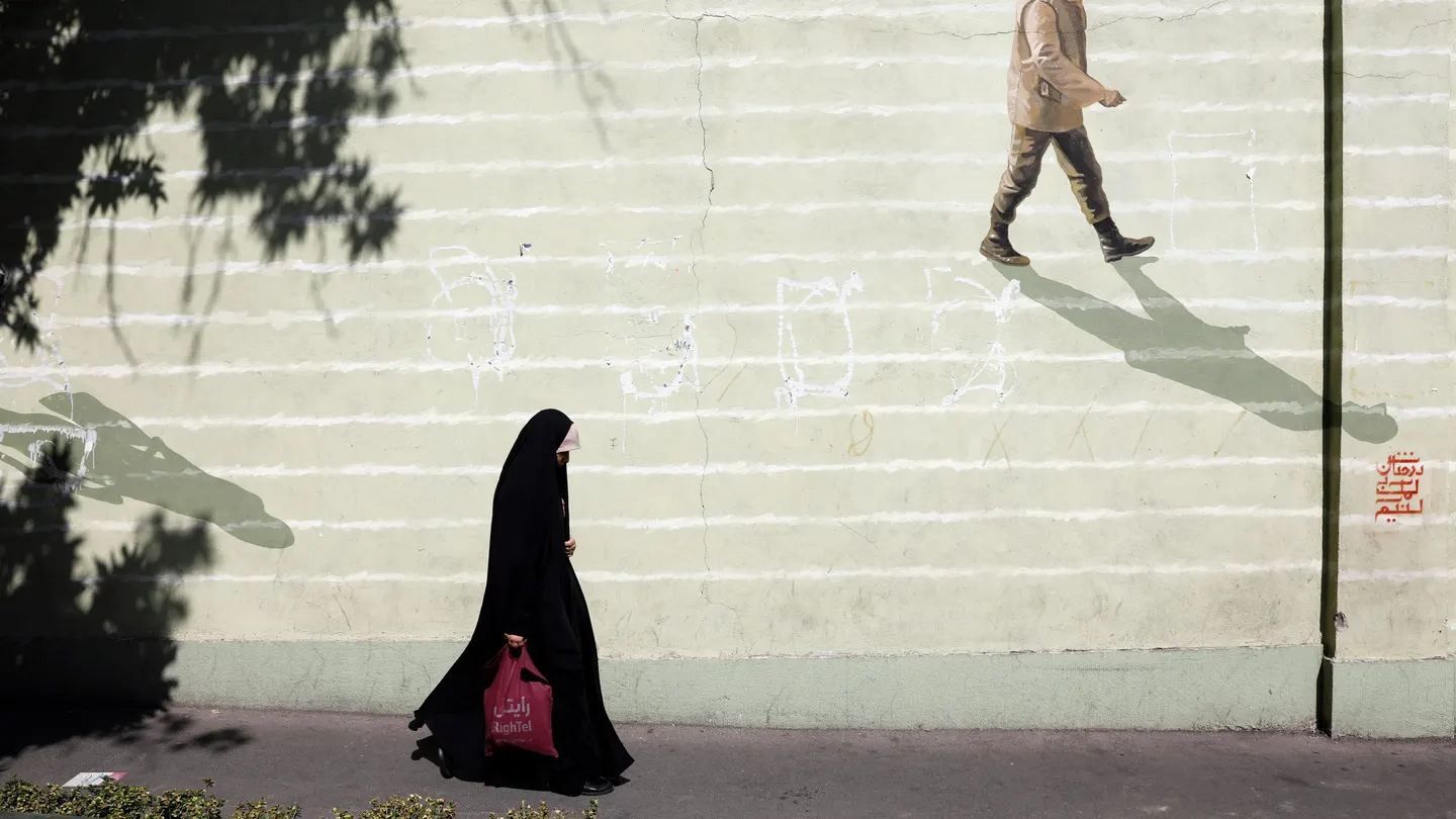 Imagen de archivo de una mujer iraní con velo que pasa junto a una pared con un soldado iraní pintado en ella en una calle de Teherán. Imagen de archivo de una mujer iraní con velo que pasa junto a una pared con un soldado iraní pintado en ella en una calle de Teherán.