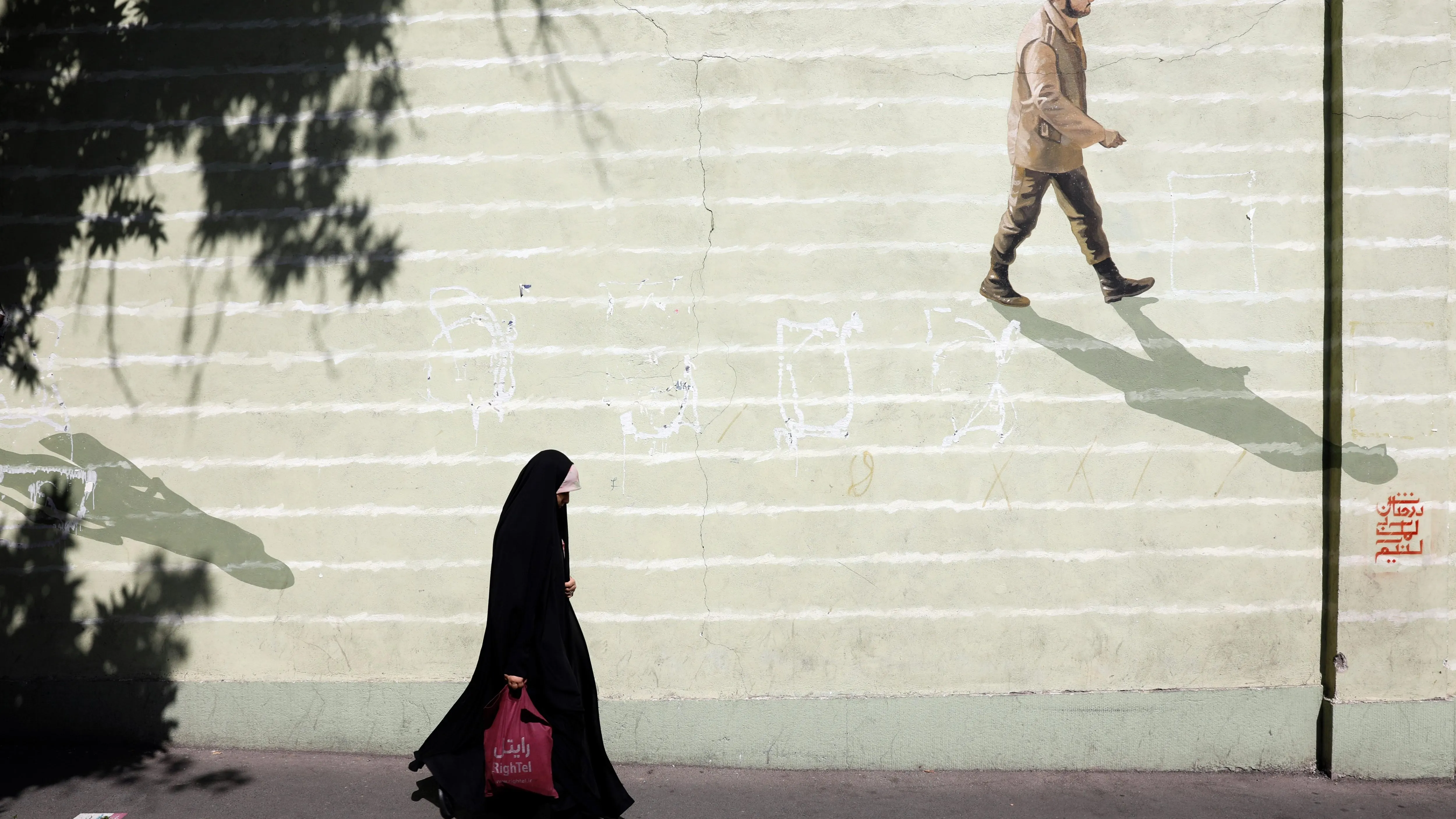 Imagen de archivo de una mujer iraní con velo que pasa junto a una pared con un soldado iraní pintado en ella en una calle de Teherán. 