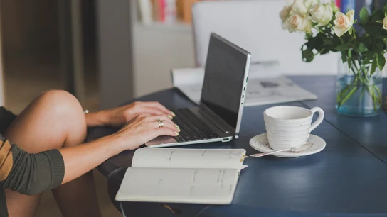 Una persona trabajando en remoto con su ordenador y un café sobre la mesa. Una persona trabajando en remoto con su ordenador y un café sobre la mesa.