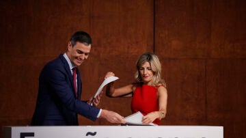 Pedro Sánchez y Yolanda Díaz intercambiándose los documentos del acuerdo firmado por ambos