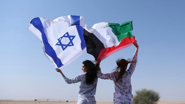Dos mujeres, cada una con una bandera: a la izquierda, la israelí; a la derecha, la palestina