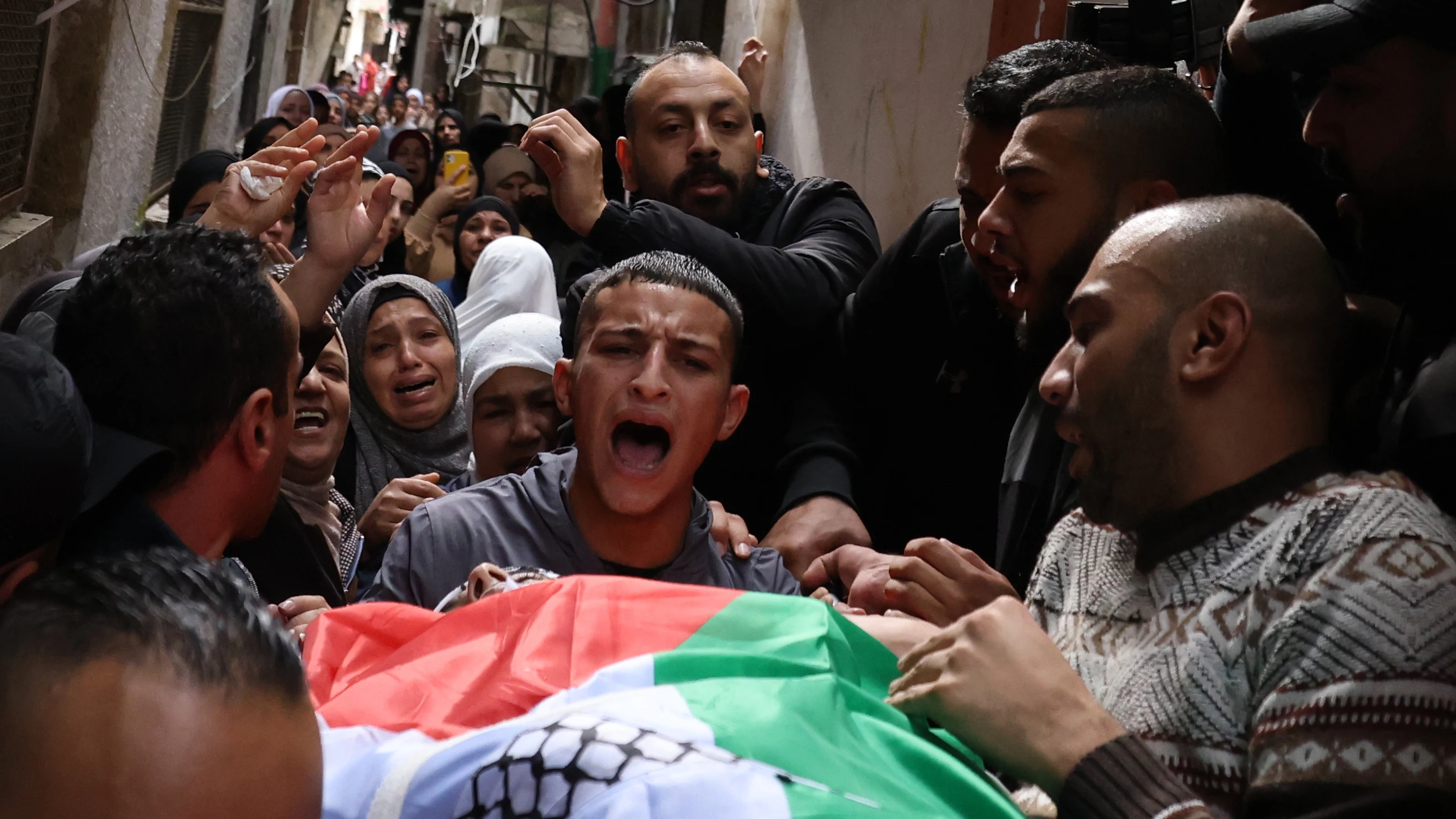 Ciudadanos sacan el cuerpo de un fallecido por los bombardeos con una bandera de Palestina