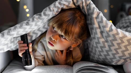 Niña leyendo bajo la manta.  Niña leyendo bajo la manta.