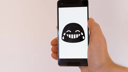 Una persona sujeta un móvil con un emoji que llora de risa. Una persona sujeta un móvil con un emoji que llora de risa.