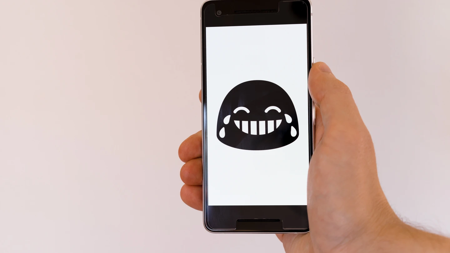 Una persona sujeta un móvil con un emoji que llora de risa. Una persona sujeta un móvil con un emoji que llora de risa.
