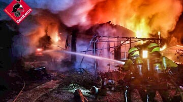 Bomberos intentan apagar el fuego en una casa incendiada en un camping de Benidoleig (Alicante)