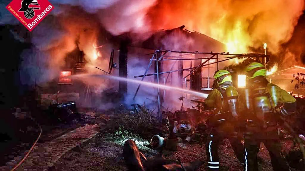 Bomberos intentan apagar el fuego en una casa incendiada en un camping de Benidoleig (Alicante)