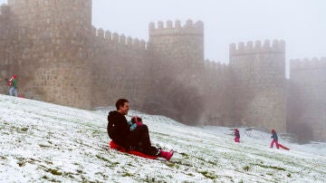 Un hombre se desliza en trineo junto a la muralla de Ávila cubierta por la nieve y el hielo 