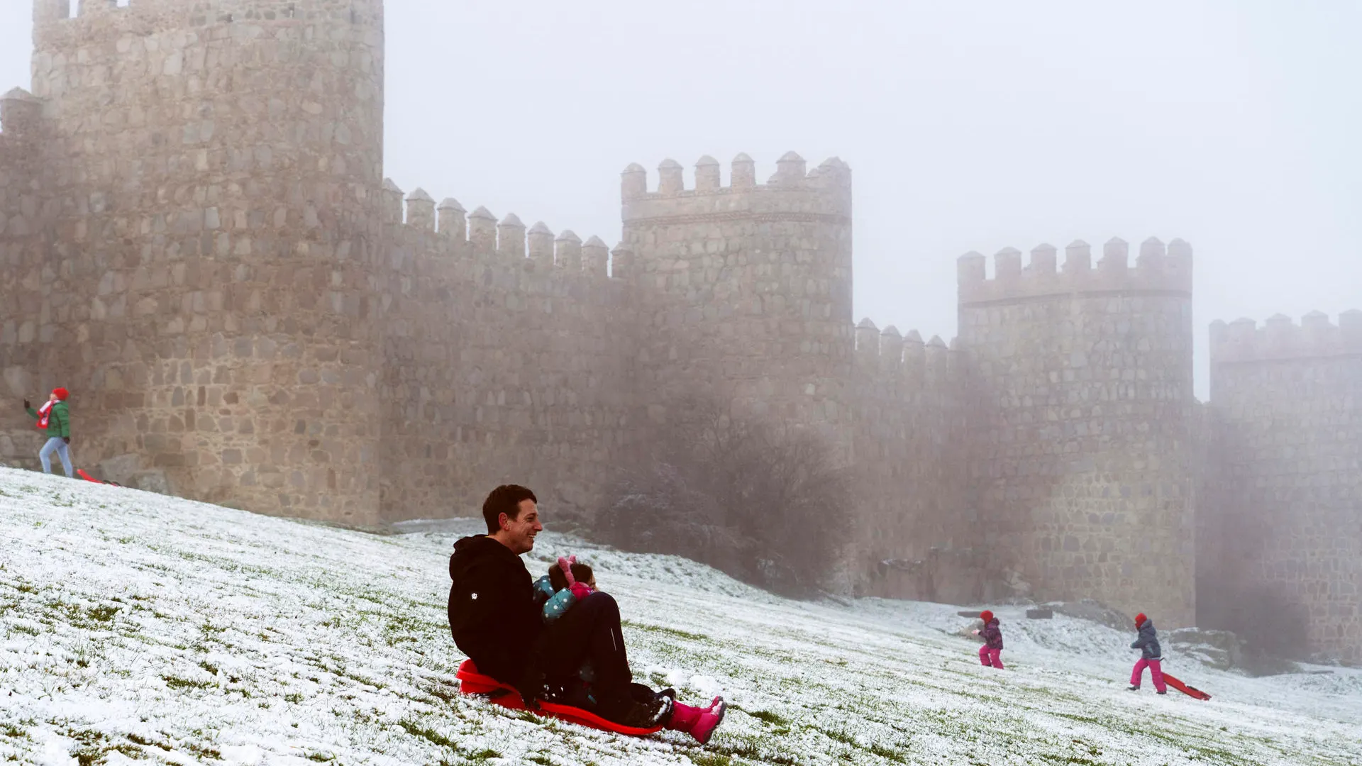 Un hombre se desliza en trineo junto a la muralla de Ávila cubierta por la nieve y el hielo 