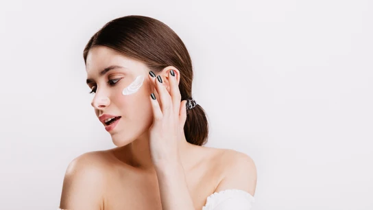 Una mujer aplicándose una crema y cosmético en la cara. Una mujer aplicándose una crema y cosmético en la cara.