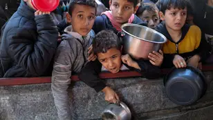 Niños palestinos esperan recibir comida cocinada en una cocina benéfica en medio de escasez de suministros alimentarios