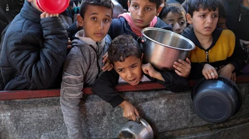 Niños palestinos esperan recibir comida cocinada en una cocina benéfica en medio de escasez de suministros alimentarios