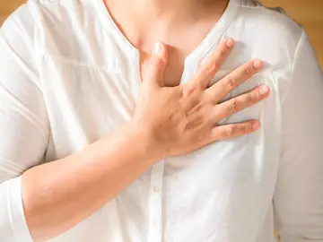 Una mujer con la mano en el pecho. El dolor en el pecho es el síntoma más común del infarto en hombres y en mujeres
