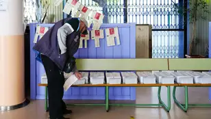 Una persona en un colegio electoral catalán, eligiendo papeleta para votar el 12M