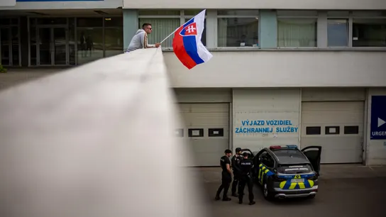 Un hombre ondea la bandera nacional eslovaca mientras un coche de policía está estacionado frente al Hospital Universitario F. D. Roosevelt, donde se encuentra el primer ministro eslovaco, Robert Fico. Un hombre ondea la bandera nacional eslovaca mientras un coche de policía está estacionado frente al Hospital Universitario F. D. Roosevelt, donde se encuentra el primer ministro eslovaco, Robert Fico.