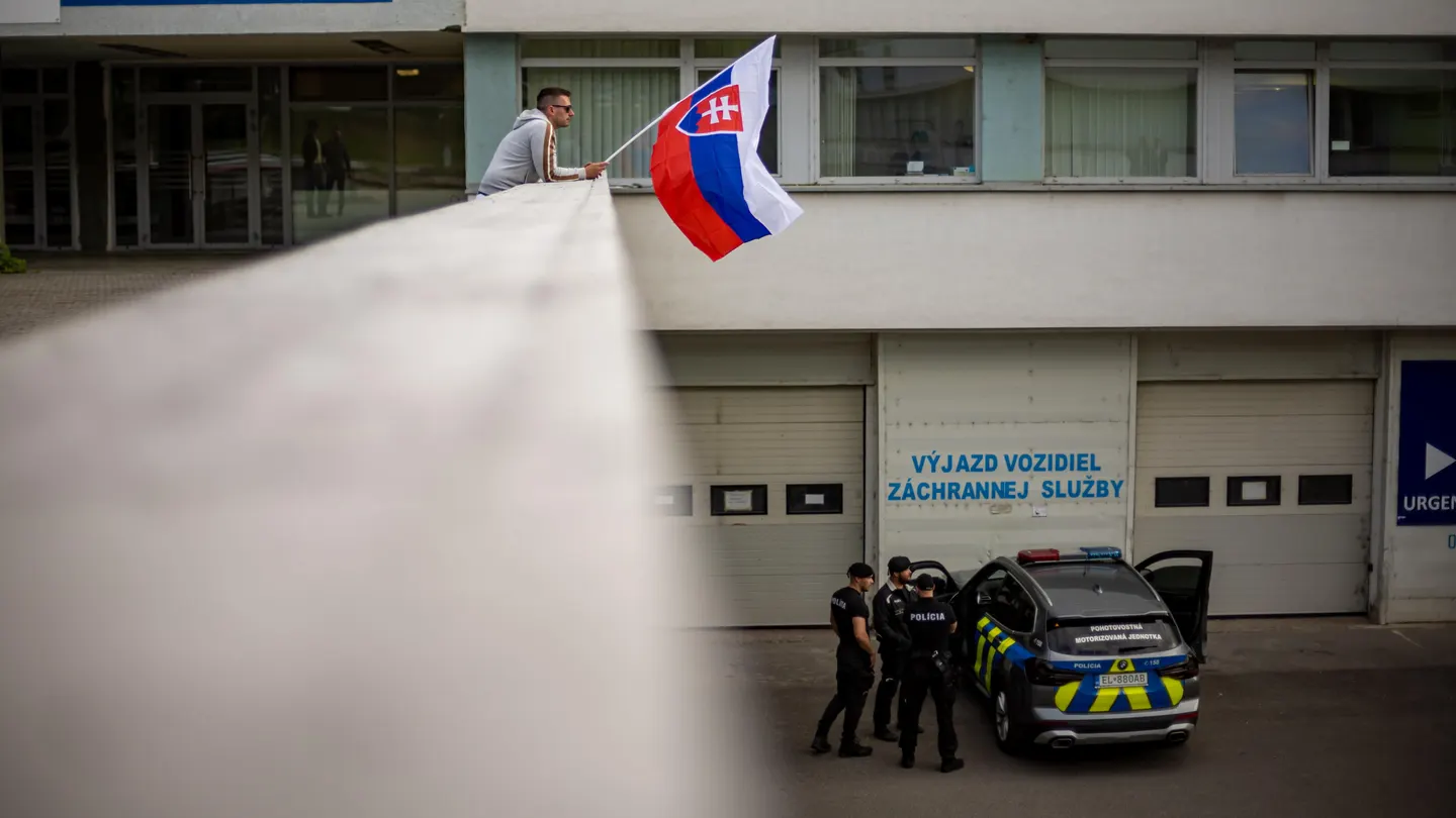 Un hombre ondea la bandera nacional eslovaca mientras un coche de policía está estacionado frente al Hospital Universitario F. D. Roosevelt, donde se encuentra el primer ministro eslovaco, Robert Fico. Un hombre ondea la bandera nacional eslovaca mientras un coche de policía está estacionado frente al Hospital Universitario F. D. Roosevelt, donde se encuentra el primer ministro eslovaco, Robert Fico.