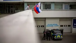 Un hombre ondea la bandera nacional eslovaca mientras un coche de policía está estacionado frente al Hospital Universitario F. D. Roosevelt, donde se encuentra el primer ministro eslovaco, Robert Fico.
