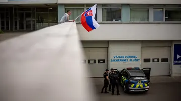 Un hombre ondea la bandera nacional eslovaca mientras un coche de policía está estacionado frente al Hospital Universitario F. D. Roosevelt, donde se encuentra el primer ministro eslovaco, Robert Fico.