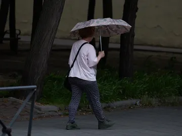Una mujer utiliza un paraguas para protegerse de la lluvia Una mujer utiliza un paraguas para protegerse de la lluvia