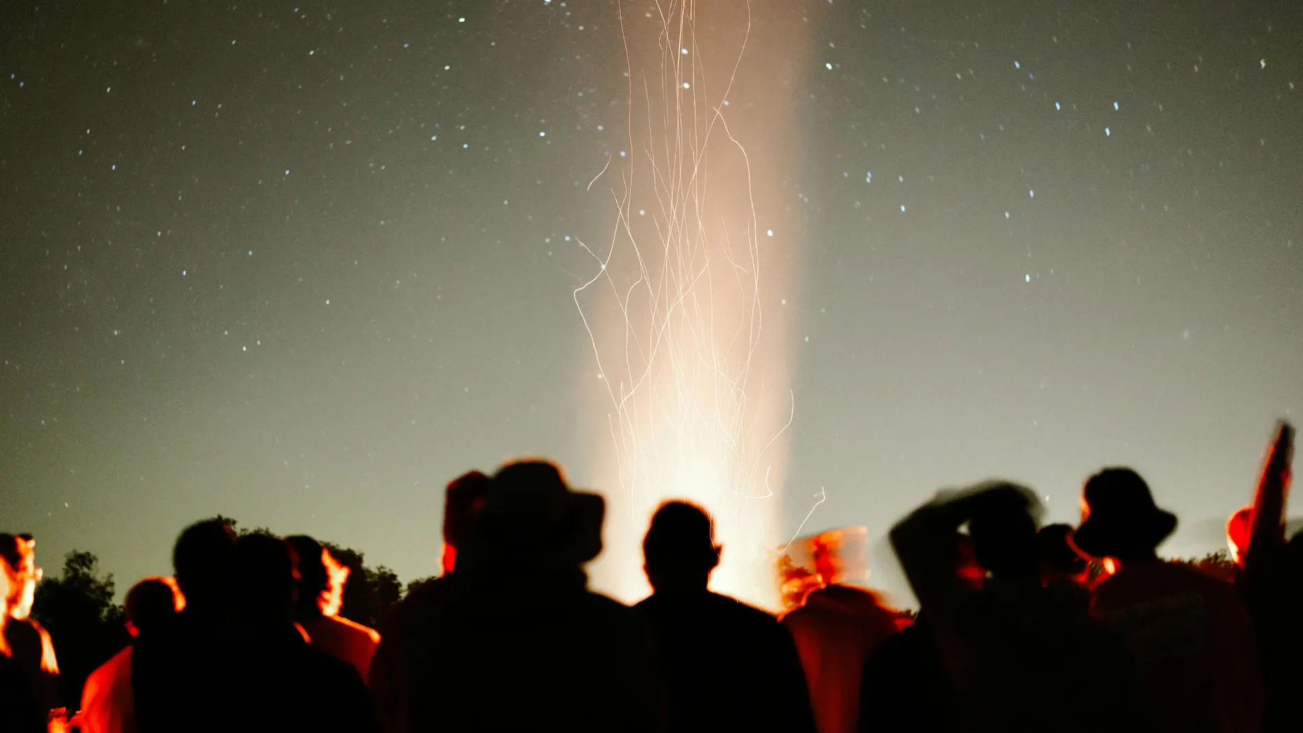 Varias personas en torno a una hoguera bajo un cielo nocturno estrellado