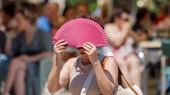 Una mujer se protege con un abanico del sol y del calor Una mujer se protege con un abanico del sol y del calor