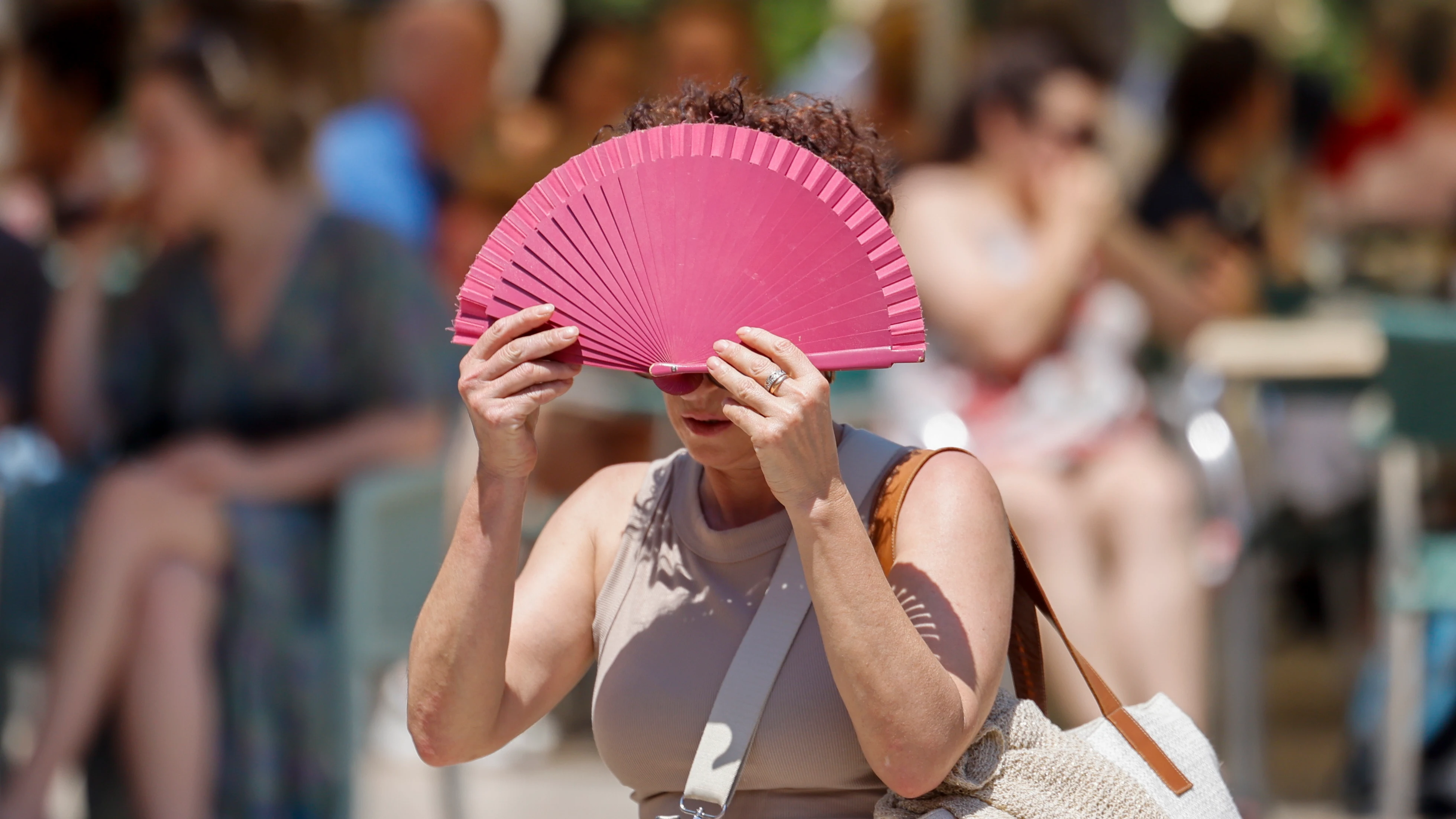 Una mujer se protege con un abanico del sol y del calor