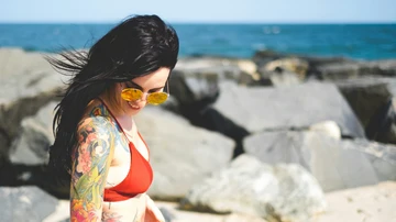 Una mujer con tatuajes de colores, en la playa.