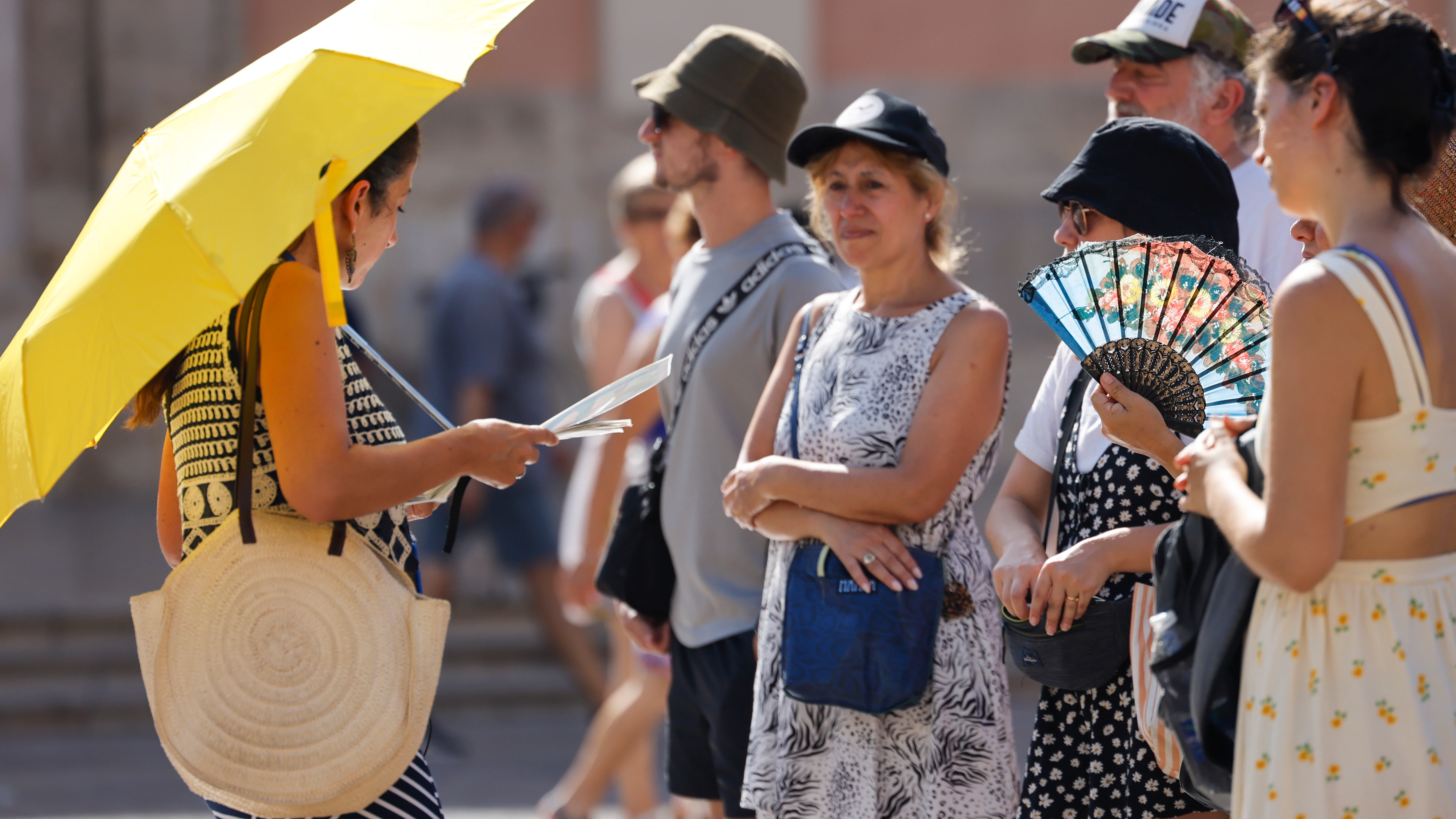 Un grupo de personas se protege del calor con parasol, abanico y gorras en la ciudad de València.