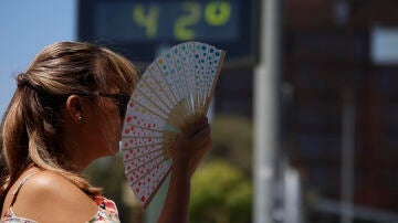 Una mujer se abanica junto a un termómetro de calle que marca 42 grados en Córdoba.