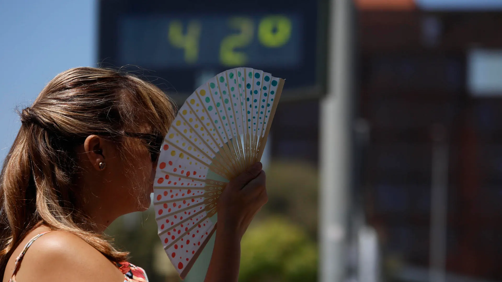 Una mujer se abanica junto a un termómetro de calle que marca 42 grados en Córdoba.