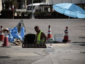 Un trabajador se protege del sol con una sombrilla en Valencia. 