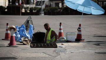 Un trabajador se protege del sol con una sombrilla en Valencia. 