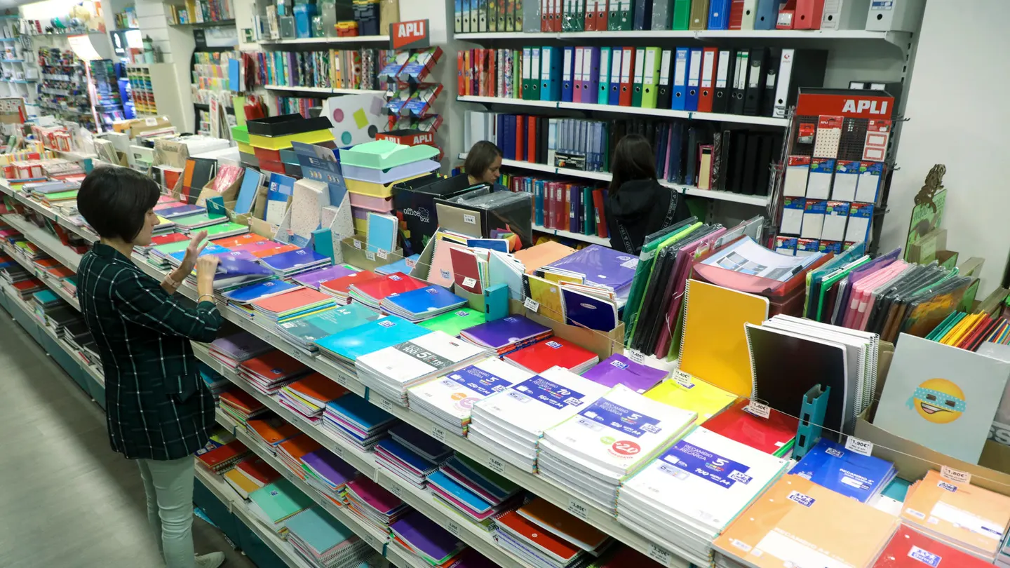 Trucos para ahorrar en la 'vuelta al cole' ante la subida de precios sin que falte de nada. Una mujer mira el material escolar ante la vuelta al cole en una papelería llena de cuadernos.