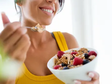 Una mujer desayunando un bol de fruta y cereales Una mujer desayunando un bol de fruta y cereales
