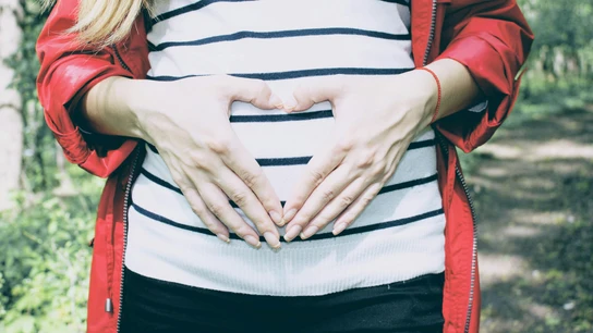 Una mujer embarazada hace la forma de un corazón con sus manos sobre su vientre. Una mujer embarazada hace la forma de un corazón con sus manos sobre su vientre.