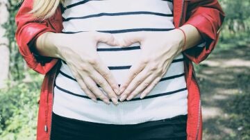 Una mujer embarazada hace la forma de un corazón con sus manos sobre su vientre.