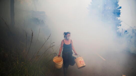 Una mujer carga cubos mientras los vecinos luchan contra el incendio en Sever do Vouga (Aveiro), este martes.
