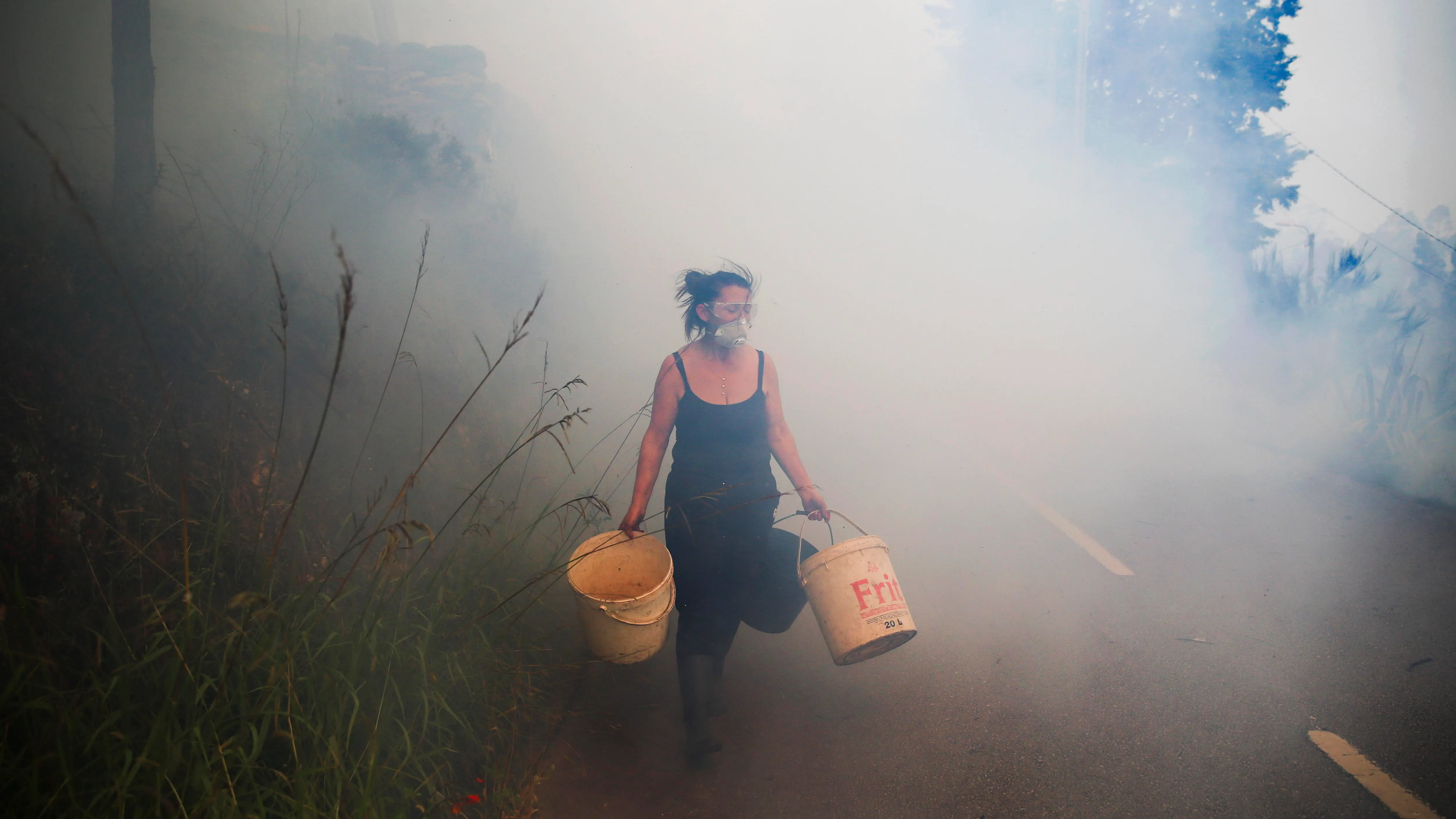 Una mujer carga cubos mientras los vecinos luchan contra el incendio en Sever do Vouga (Aveiro), este martes.