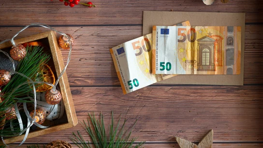 ¿Cuándo se cobra la paga extra de Navidad? Dos billetes de 50 euros, al lado de unas decoraciones navideñas.