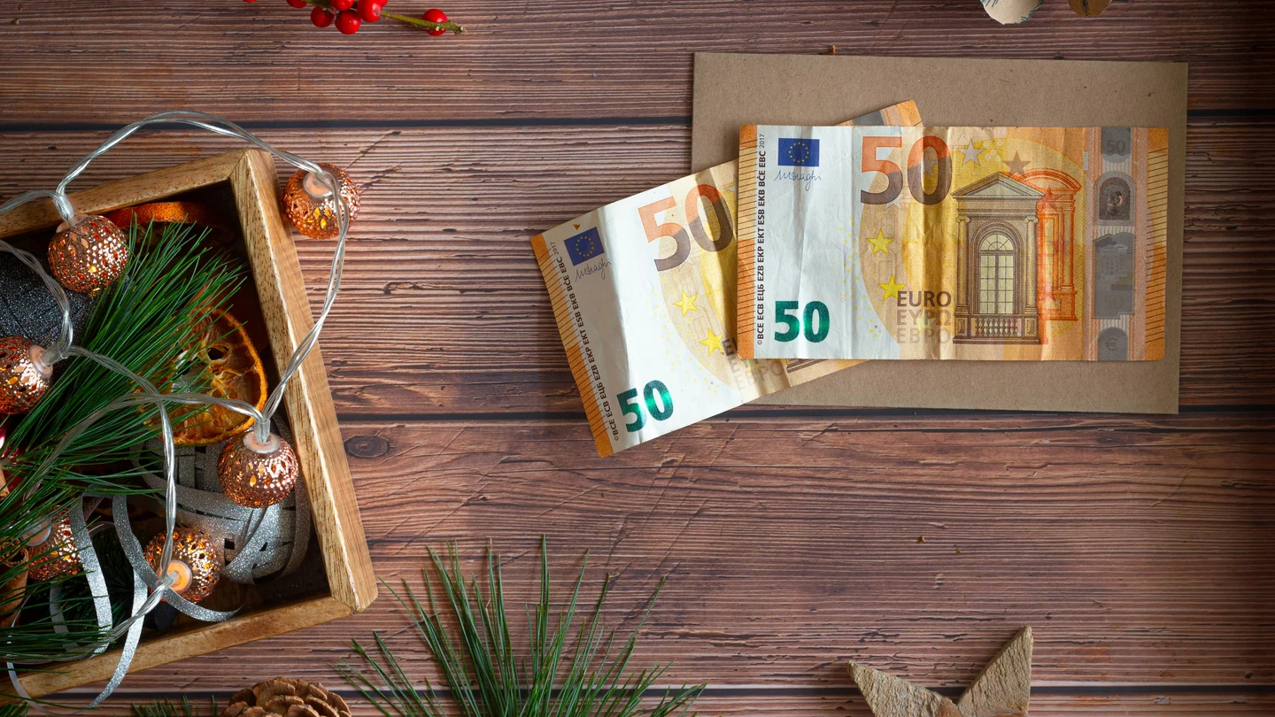 ¿Cuándo se cobra la paga extra de Navidad? Dos billetes de 50 euros, al lado de unas decoraciones navideñas.