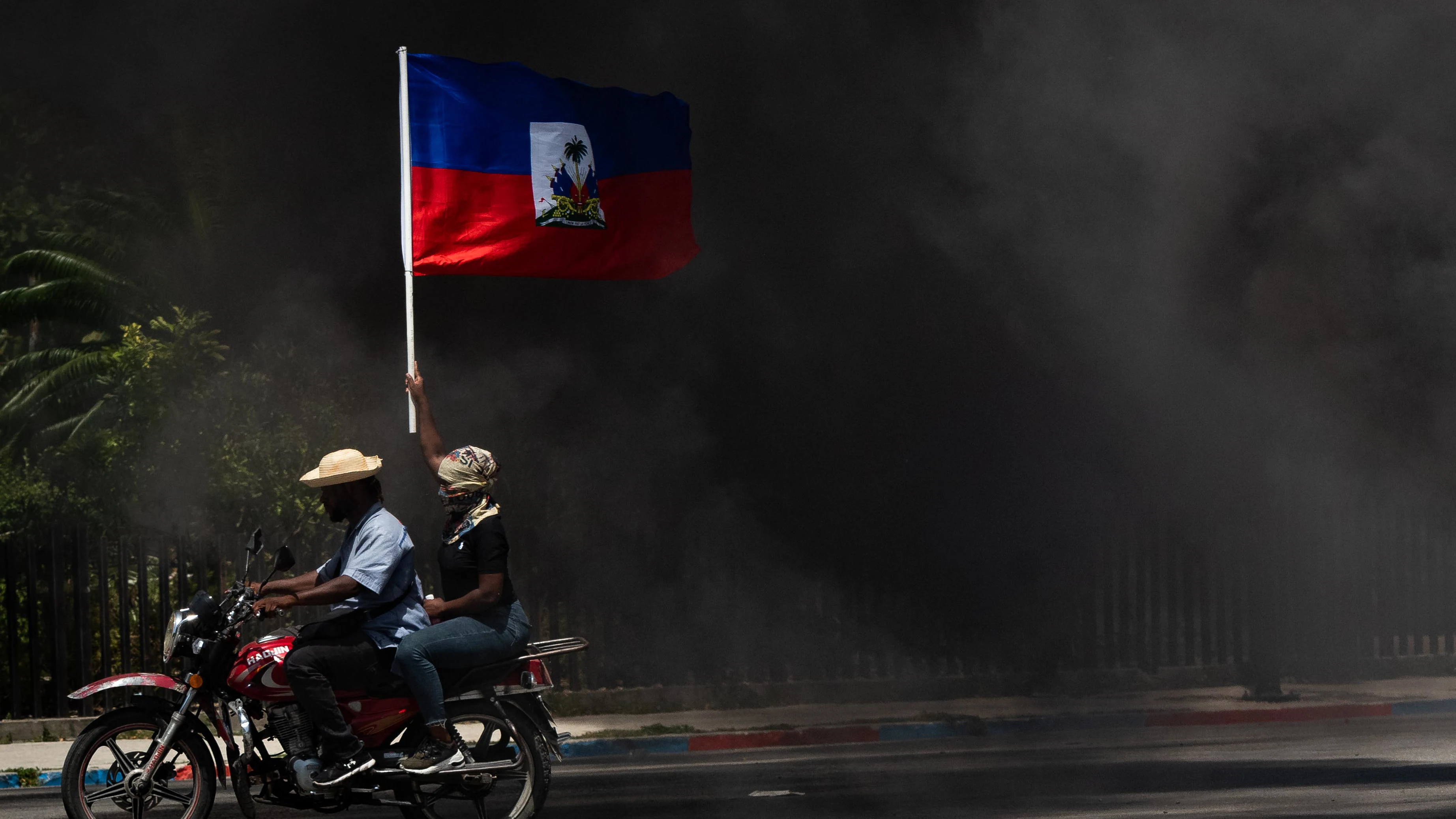 Fotografía de archivo de una persona que ondea una bandera haitiana en medio del humo, durante una marcha para exigir seguridad contra las pandillas