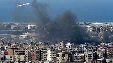 Un avión vuela en medio del humo que se eleva sobre la ciudad tras un ataque aéreo israelí en el bastión de Hizbulá