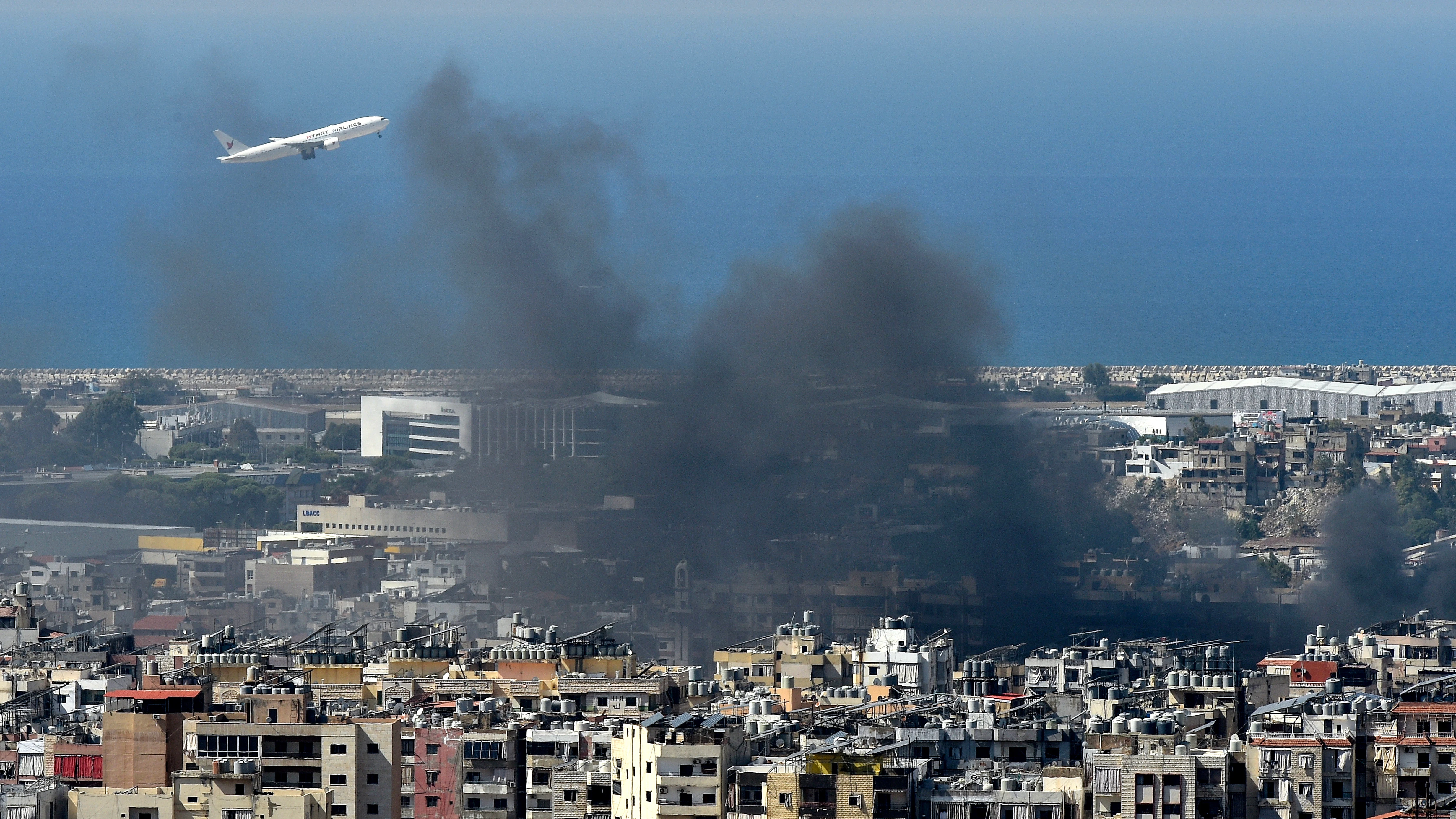 Un avión vuela en medio del humo que se eleva sobre la ciudad tras un ataque aéreo israelí en el bastión de Hizbulá