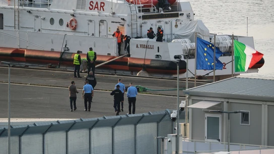Un funcionario de seguridad camina frente a un barco de la guardia costera italiana que se prepara para partir del puerto de Shengjin Un funcionario de seguridad camina frente a un barco de la guardia costera italiana que se prepara para partir del puerto de Shengjin