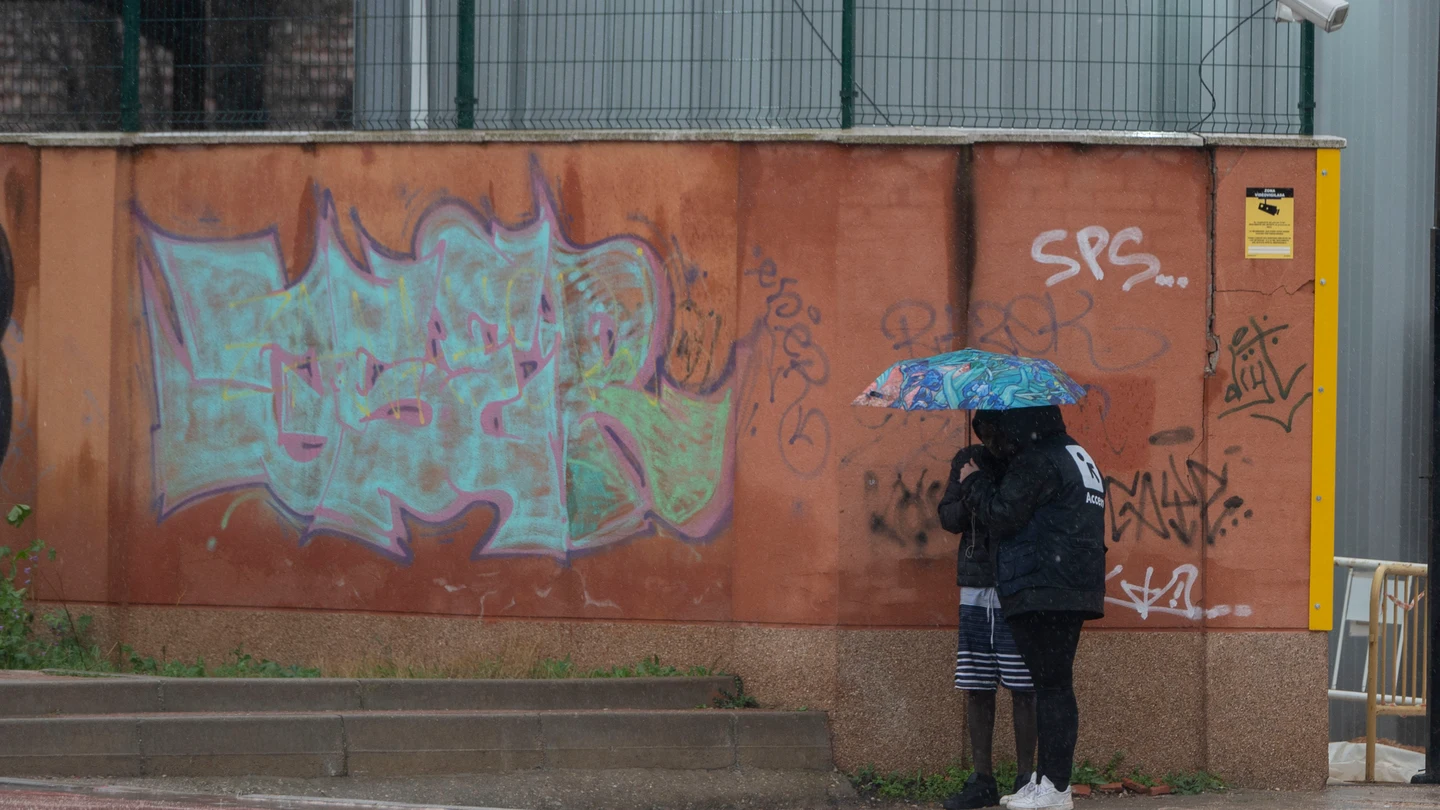 Dos migrantes se protegen de la lluvia con un paraguas en las inmediaciones del centro de Emergencia, Acogida y Derivación de Alcalá de Henares Dos migrantes se protegen de la lluvia con un paraguas en las inmediaciones del centro de Emergencia, Acogida y Derivación de Alcalá de Henares